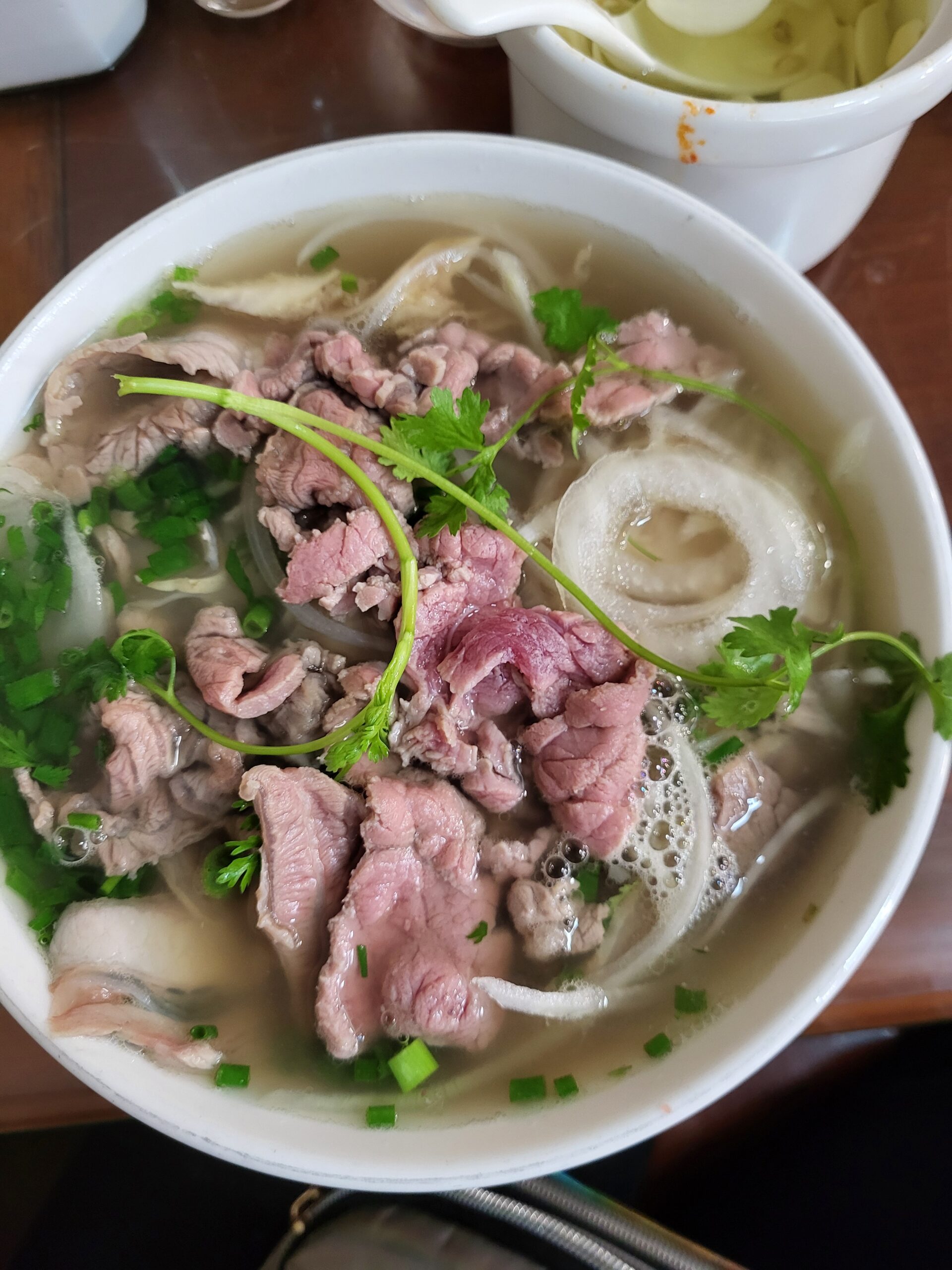 A steaming bowl of authentic Hanoi pho topped with beef, herbs, and lime at a busy local street stall.